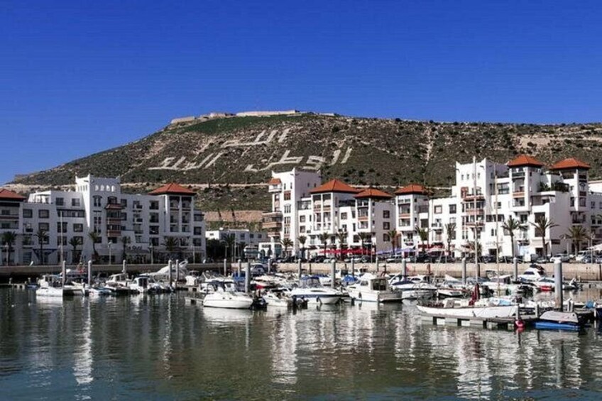 Un puerto deportivo con barcos, edificios blancos con tejados rojos y una colina al fondo. 3