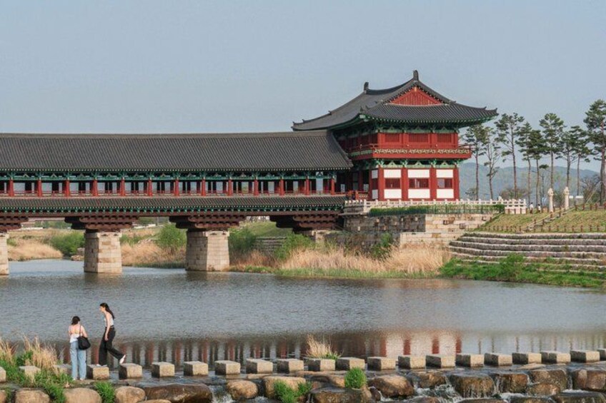 En traditionell koreansk bro över en stilla flod, med en röd och grön byggnad på höger sida. 3
