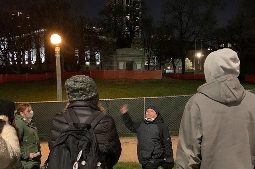 En gruppe mennesker står nær en hegn i en park om natten. 1