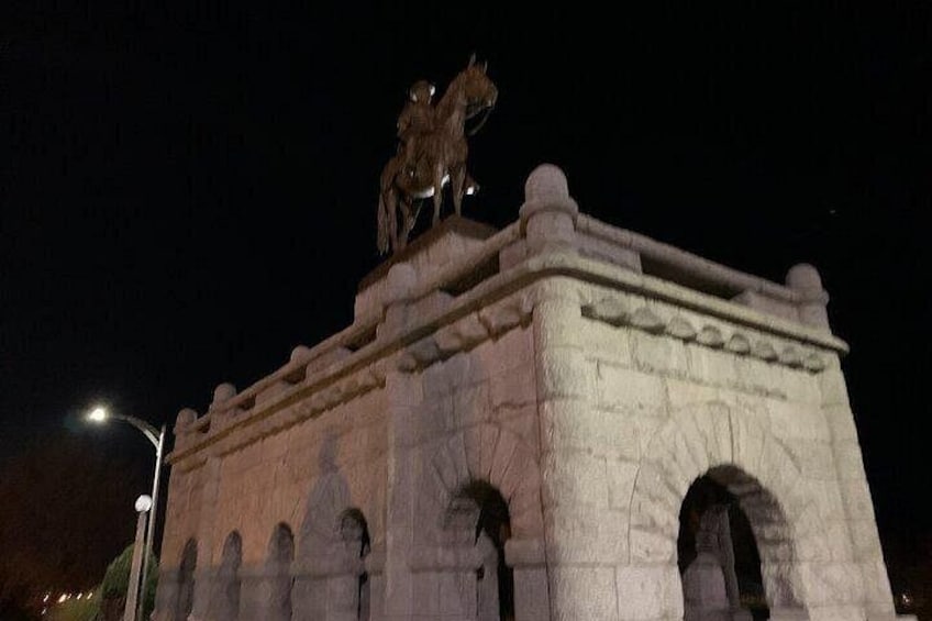 En stenhøj med en statue af en person på hesteryg, hvælvede åbninger og en lygtepæl. 2