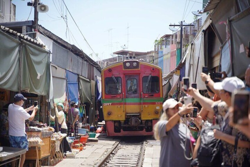 A colorful train passing through a narrow street with people taking photos. 1