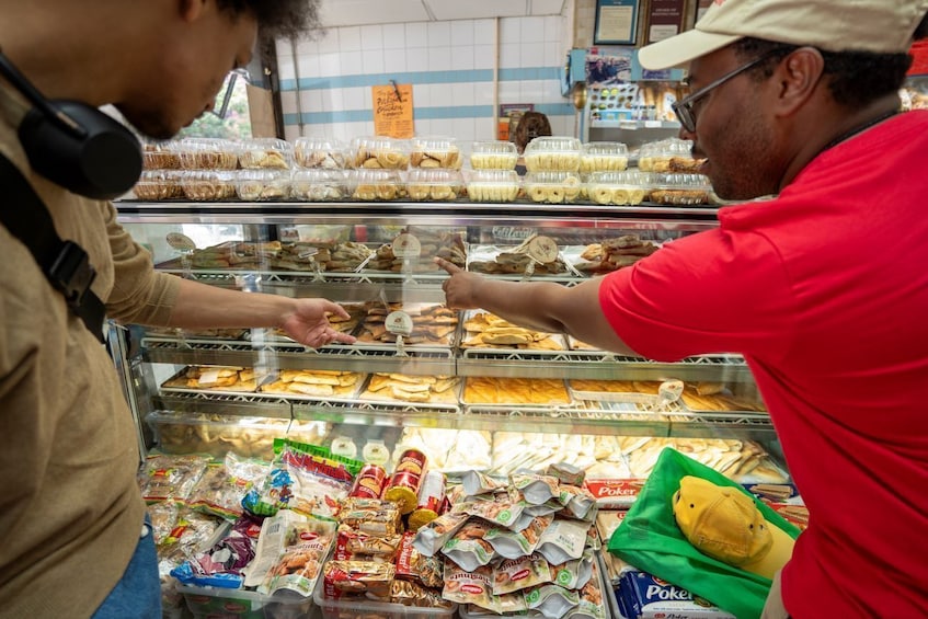 A person in a red shirt at a bakery counter selecting pastries from a display case. 1