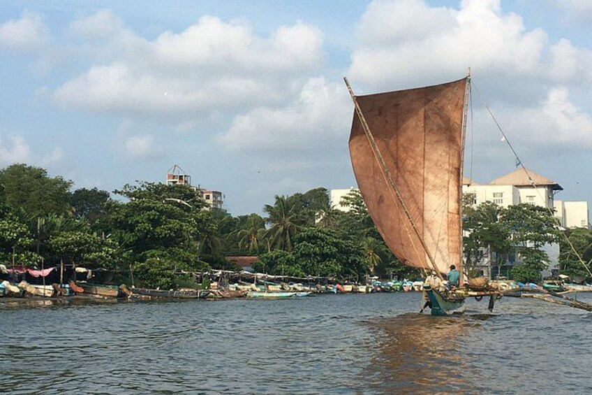 A sailboat with a large sail on the water, a dock with people, and buildings in the background. 5
