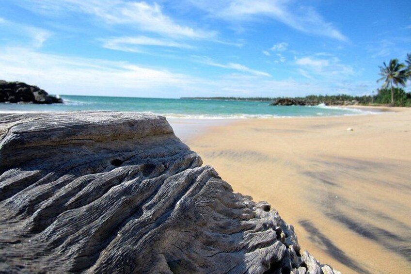 A beach with a large rock in the foreground, a sandy shore, and a clear blue sky. 2