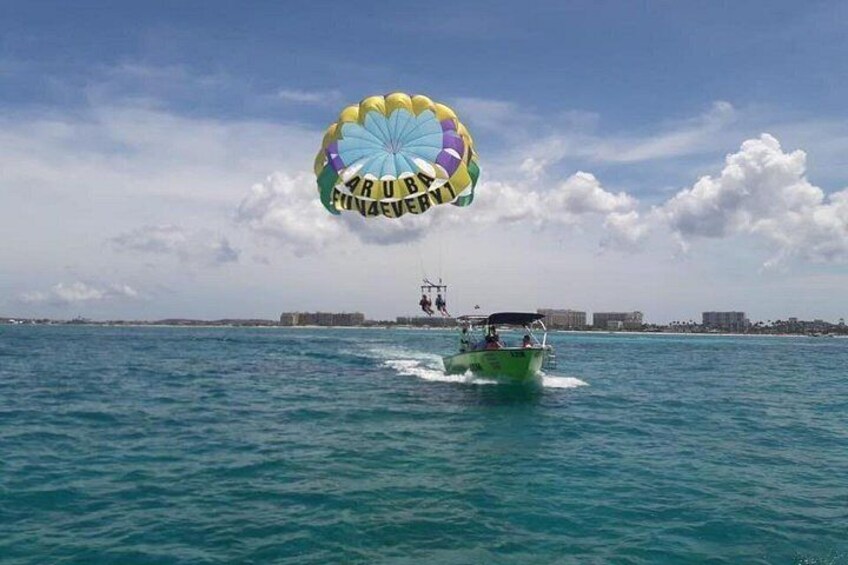 Parasailing boven turquoise water, met een boot en een paraschutje op de achtergrond. 3