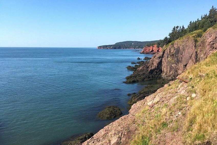 A coastal landscape with clear blue water, rocky cliffs, and a distant shoreline. 4