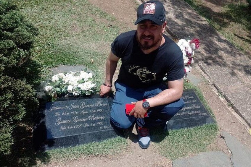 A man kneeling beside a gravestone with inscriptions, holding a red object. 4