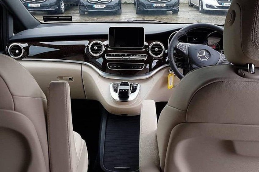 A car's interior with beige leather seats, a central console with a touchscreen display, and a steering wheel with a logo. 2