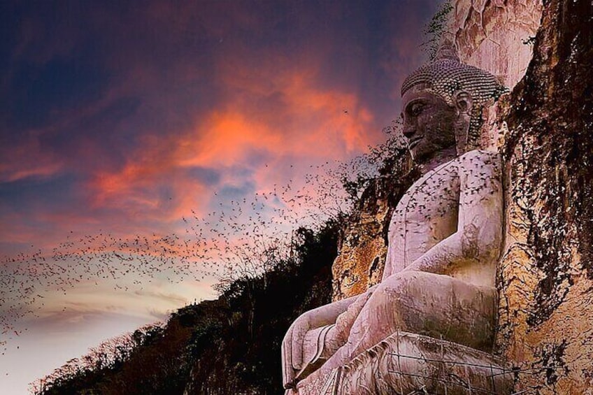 En stor Buddha-staty i solnedgången, med fåglar som flyger runt den. 2