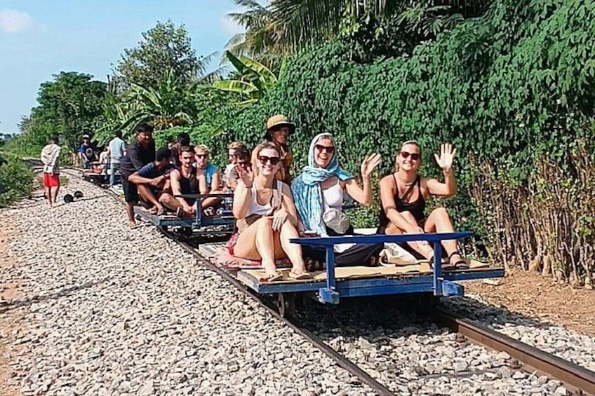 A group of people on a small train ride through a rural area with greenery and palm trees. 1