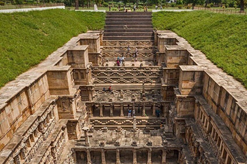 An ancient stone structure with steps leading up to a central platform, surrounded by a grassy area. 5