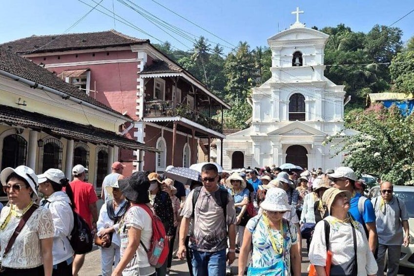 A crowd of people walking past a white church with a bell tower. 3