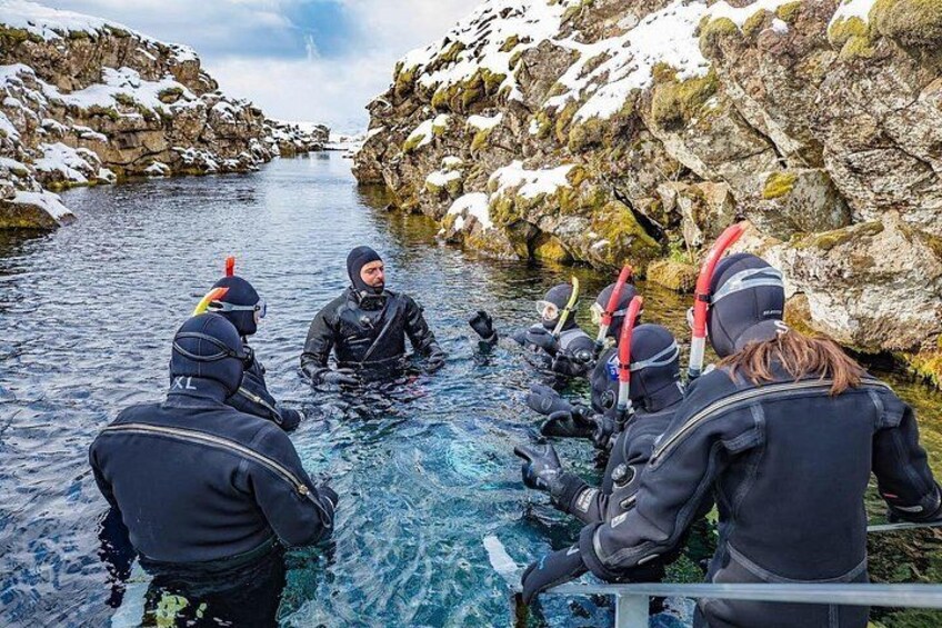 Un grupo de personas con equipo de buceo en un cuerpo de agua cristalina rodeado de terreno rocoso. 2