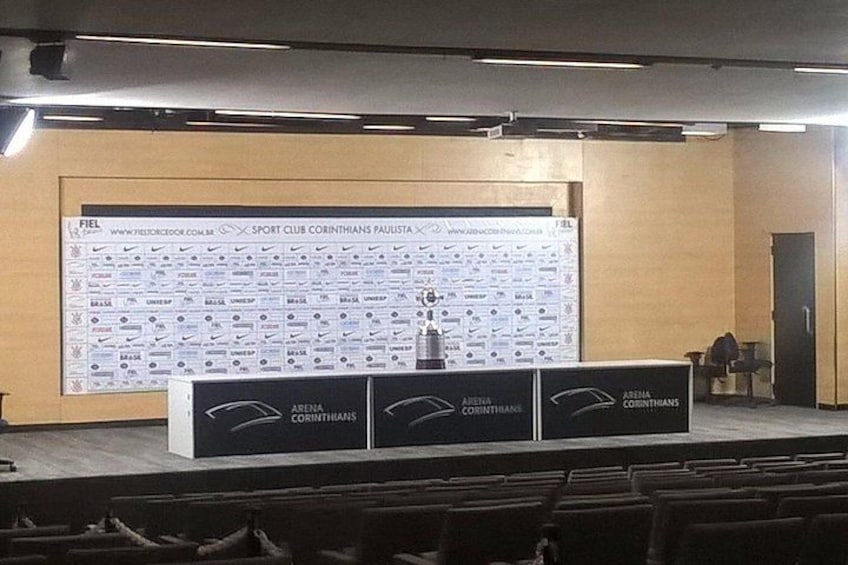 An indoor sports arena with a large display board, a podium, and rows of seats. 3
