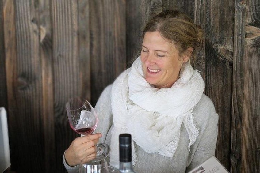 Una persona sosteniendo una copa de vino y una botella, sentada frente a un fondo de madera. 2