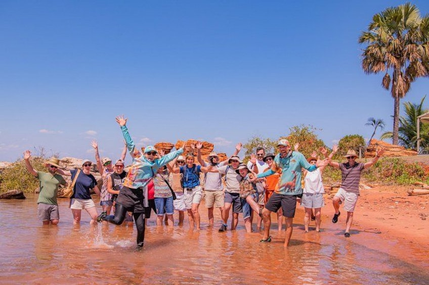 A group of people dancing in a shallow water body with palm trees and a clear sky in the background. 4