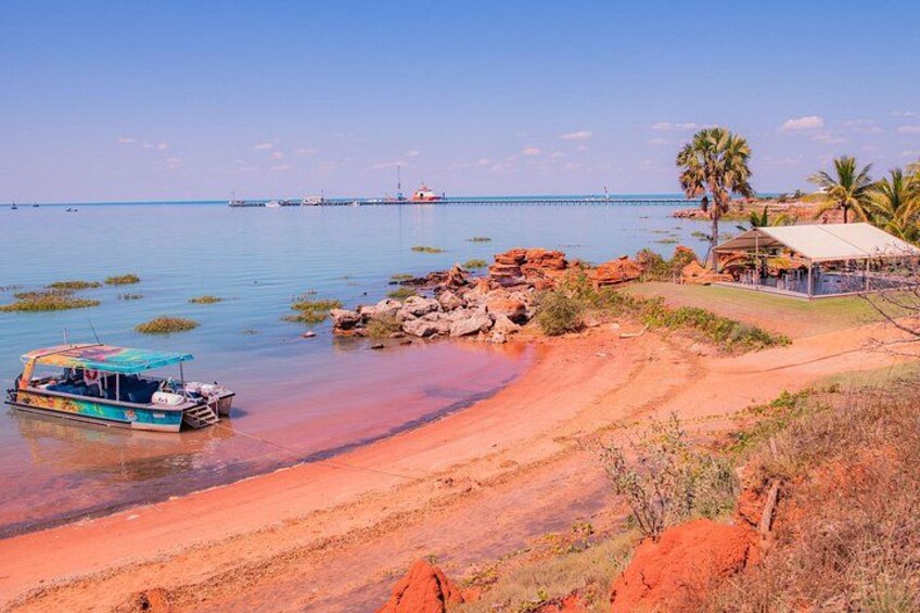 A beach with a boat, rocky shoreline, palm trees, and a distant pier. 3