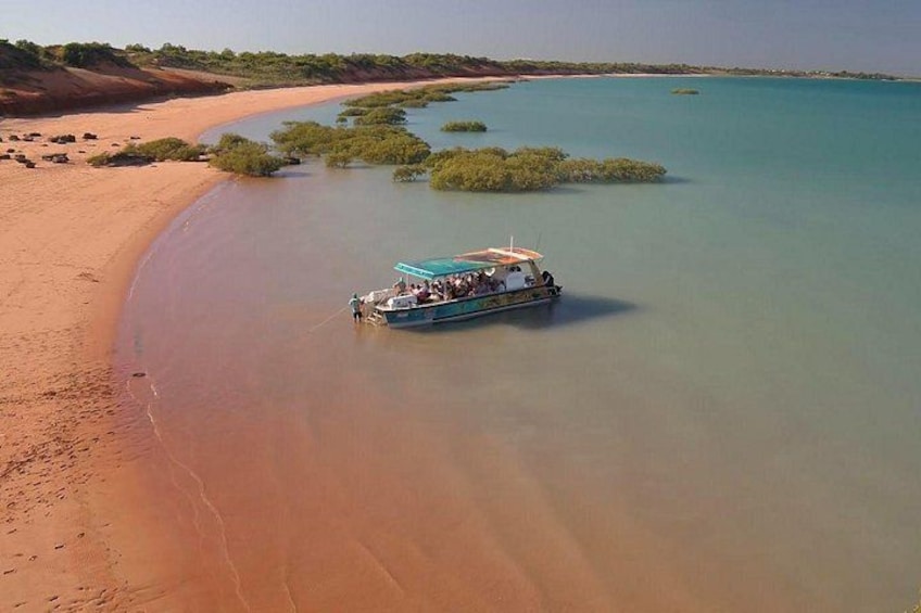 A boat on a calm riverbank with clear water and a sandy beach. 1