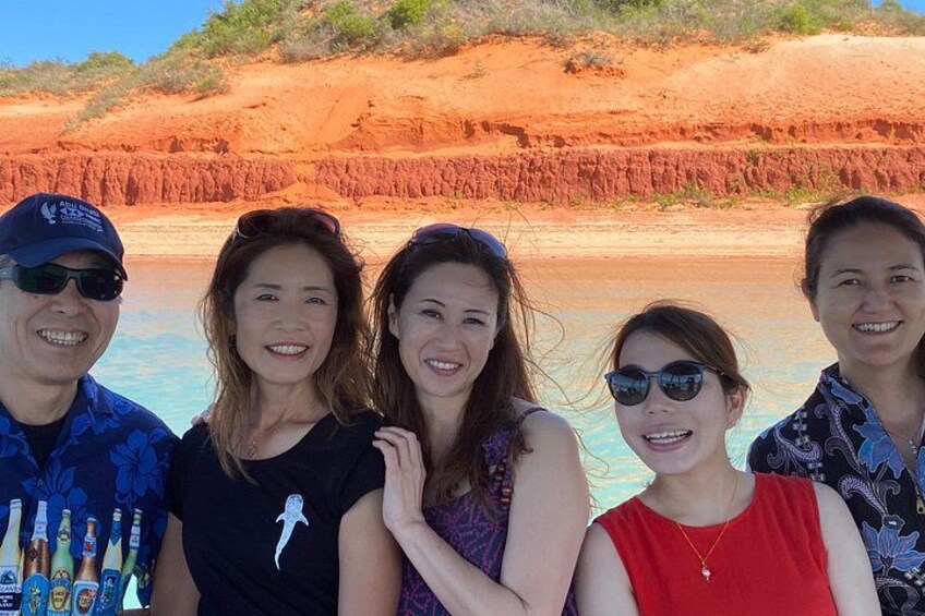 A group of people standing by a body of water with red cliffs in the background. 3