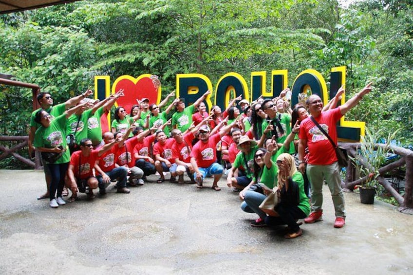 Eine Gruppe von Menschen posiert vor einem großen Schild mit dem Text 'I ♥ BOULOU'. 3