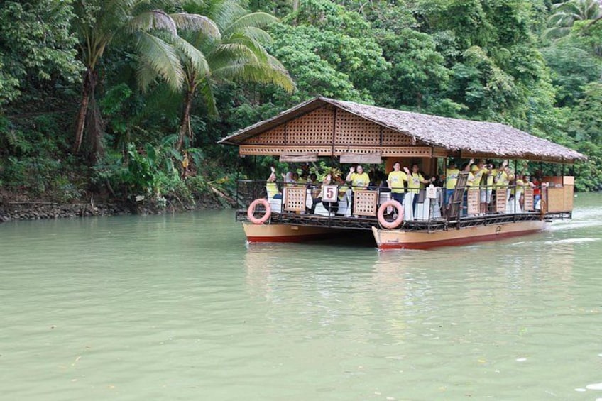 Ein Boot mit überdachter Deck und Passagieren, umgeben von dichter tropischer Vegetation. 5