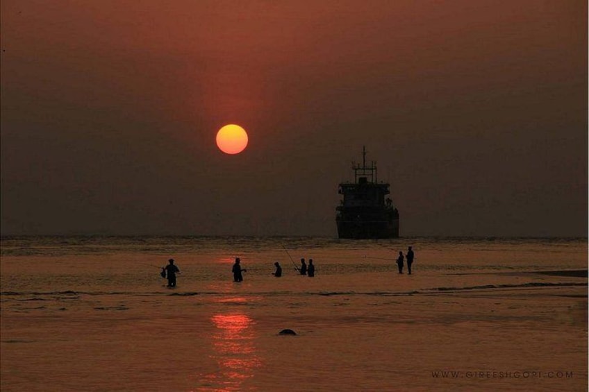 A sunset over a calm sea with a ship in the distance and people fishing on the shore. 2