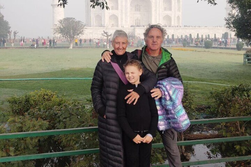 Una familia frente al Taj Mahal, con una barandilla verde y una zona arbolada en primer plano. 4