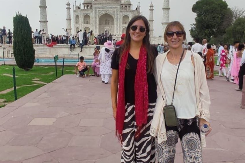 Two people standing in front of a large white building with domes and minarets, surrounded by a crowd. 3