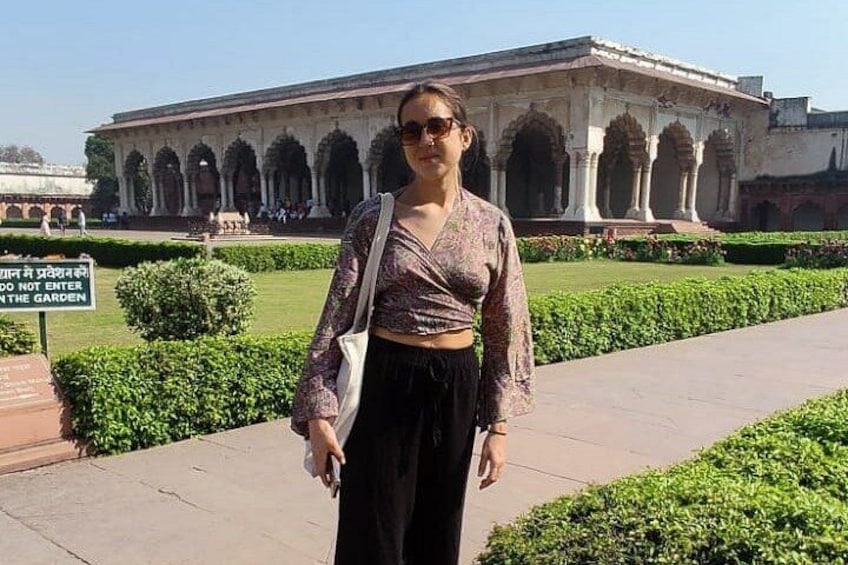 A person standing in front of a historical building with arches, a sign prohibiting entry into the garden, and well-maintained greenery. 3