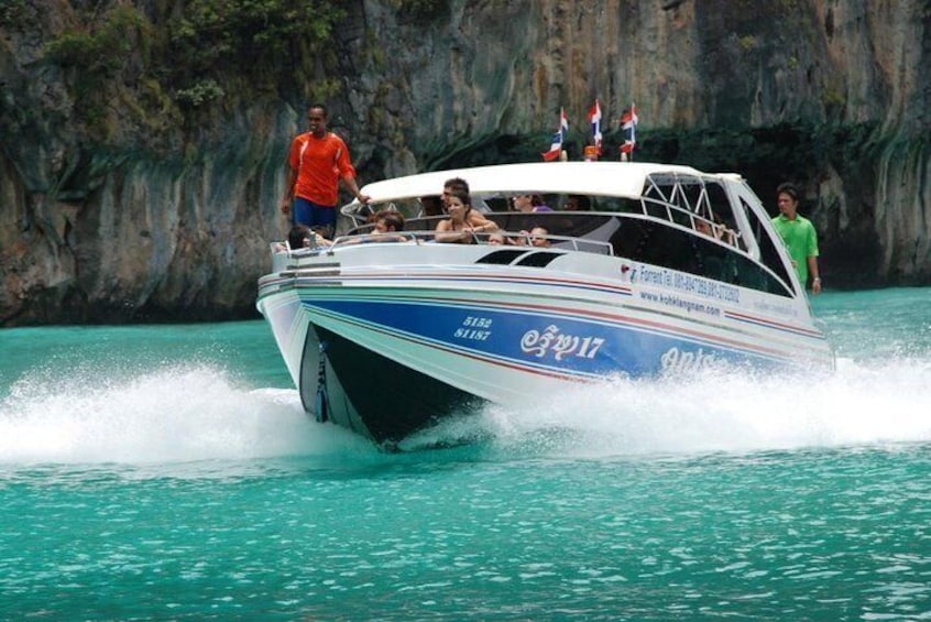 A speedboat with passengers, moving through turquoise water with a rocky cliff in the background. 1