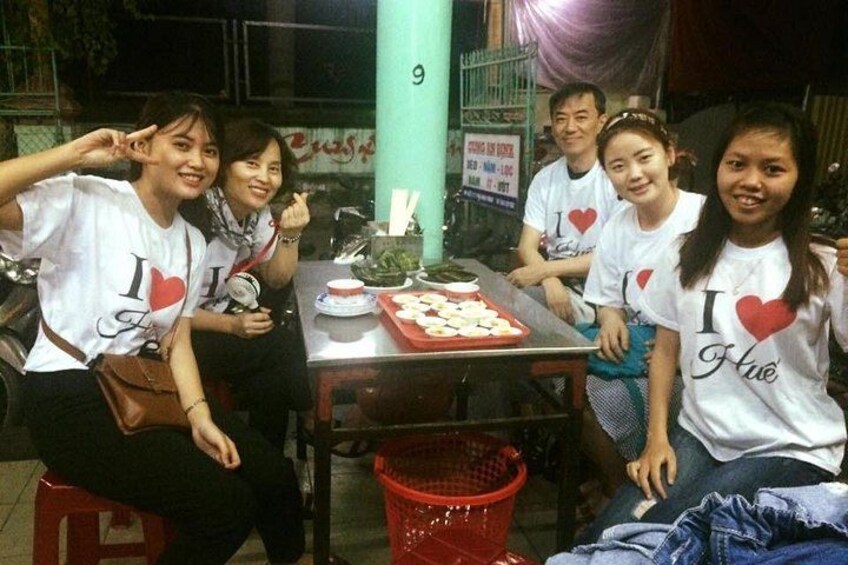 A group of people sitting at a table with food, wearing matching t-shirts with a heart symbol and text. 4