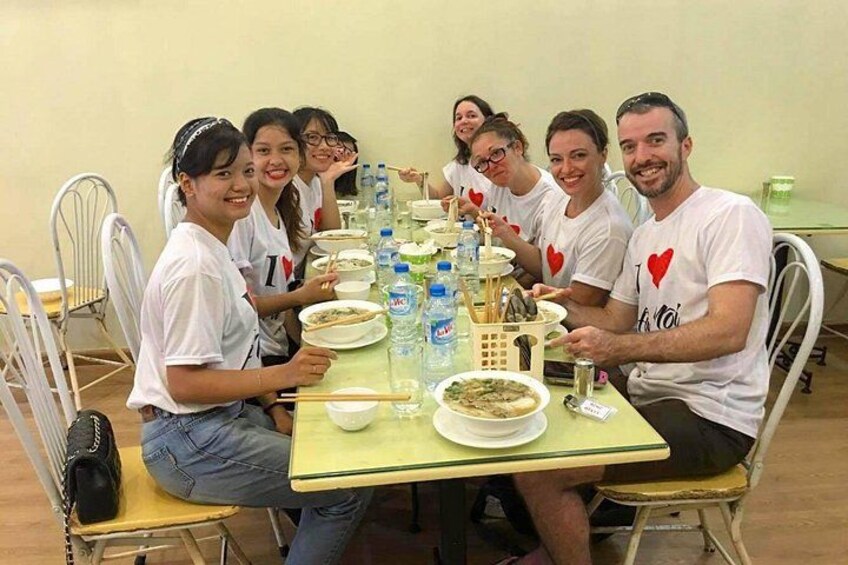 A group of people sitting around a table with plates of food, bottles of water, and a basket. 3