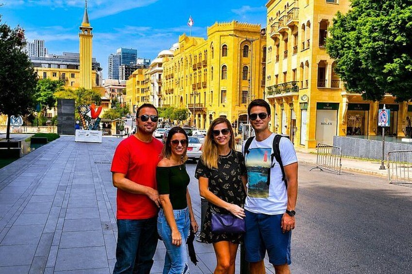Un grupo de personas de pie en una acera de la ciudad, con edificios históricos y una torre al fondo. 2
