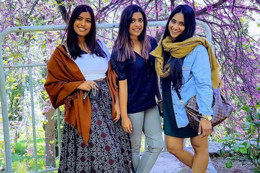 Three women standing in front of a metal fence with purple flowers in the background. 2