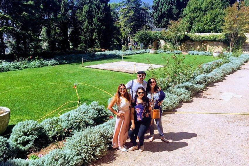 A group of people posing in a garden with a well-manicured lawn, hedges, and a gravel path. 1