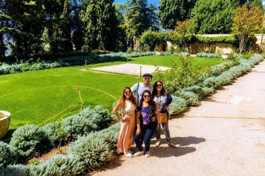 A group of people standing on a gravel path in a well-manicured garden with trimmed hedges and a lawn. 5