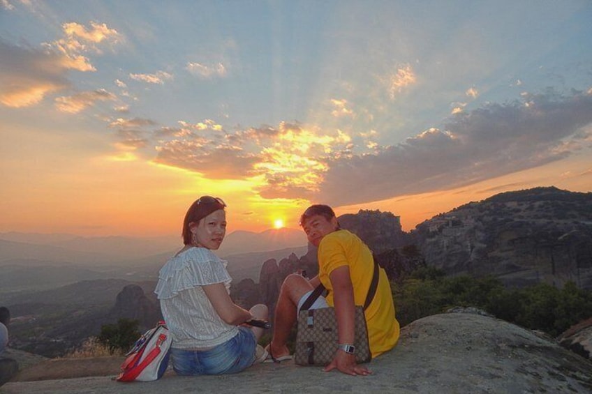 Two people sitting on a rock with a sunset in the background. 3