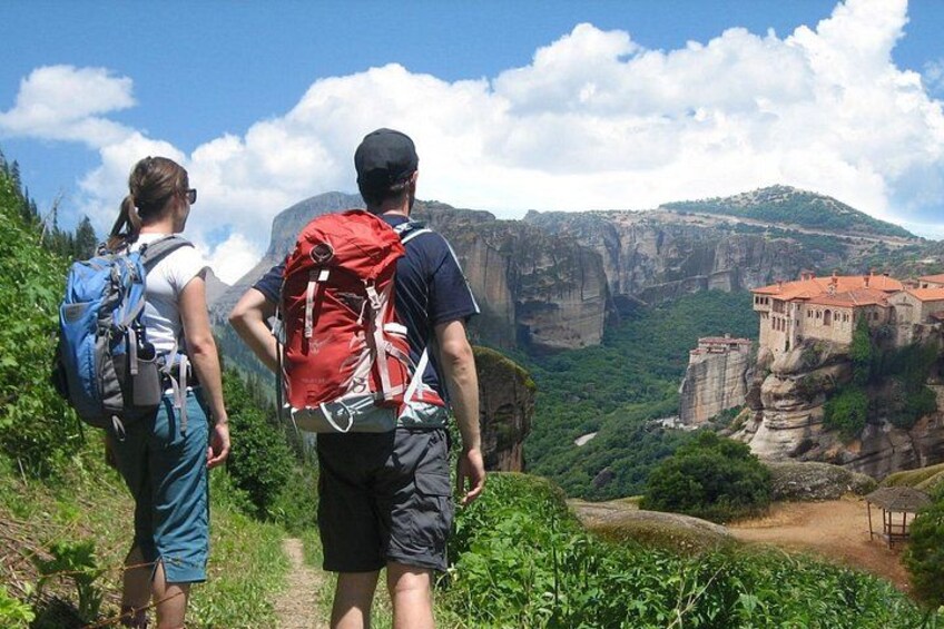 Dos excursionistas en un sendero con vistas a un edificio histórico en un acantilado. 1