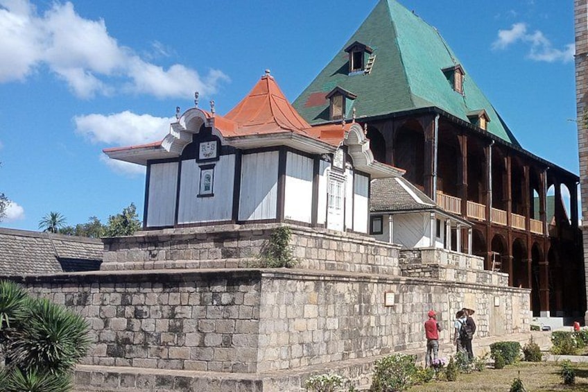 A historical building with a green roof, a white facade, and a stone base. 5