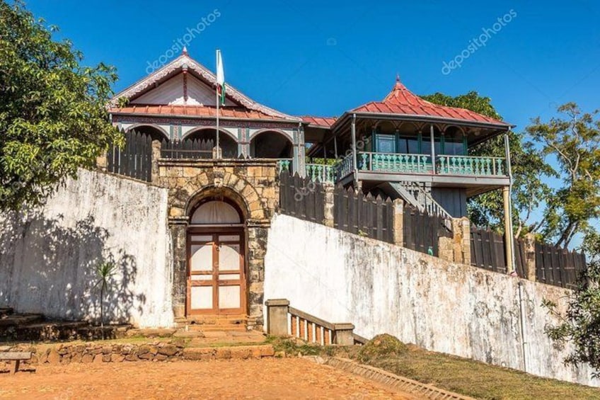 A colonial-style building with a red roof, a balcony, and a flagpole. 1
