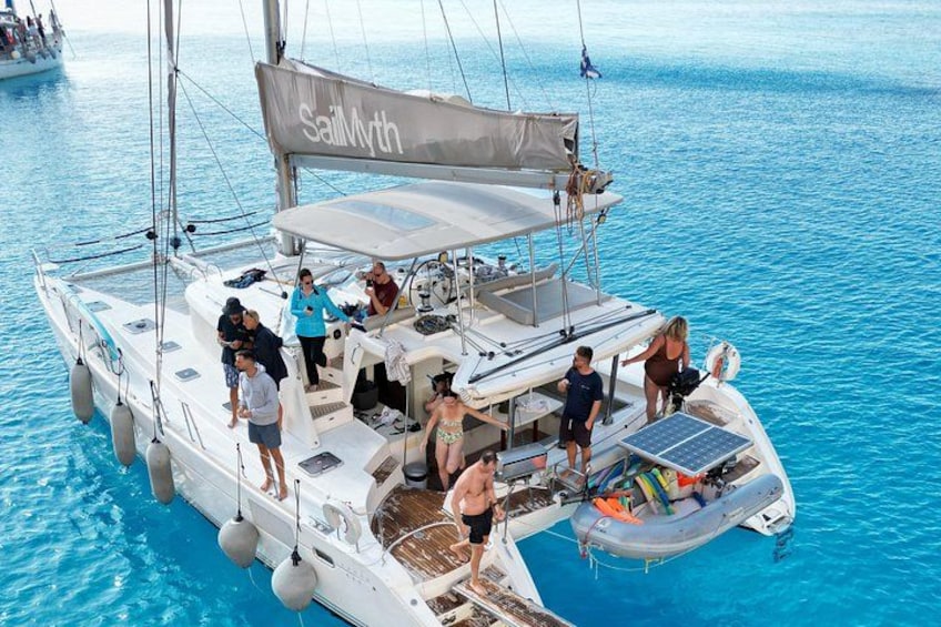 A sailboat named 'SailMyth' with people on deck, a small inflatable boat, and calm blue waters. 1