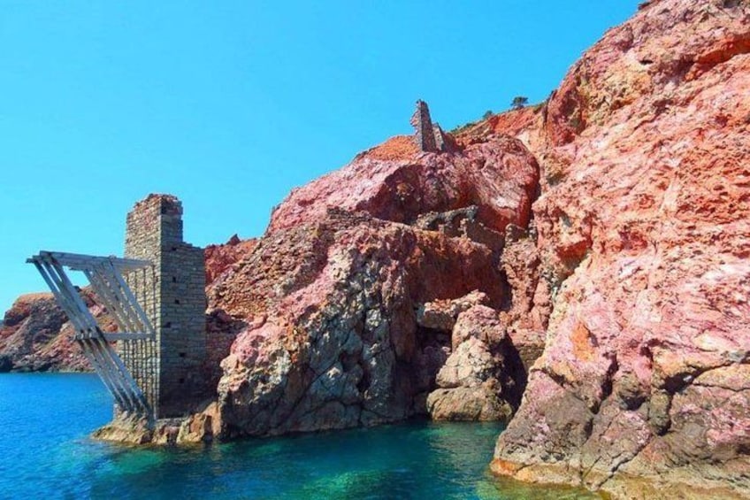 A coastal landscape with a rocky cliff, a metal gate, and clear blue water. 5