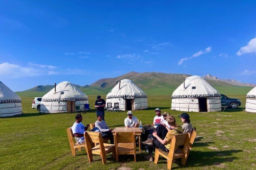 A group of people seated at a wooden table outdoors with yurts in the background. 5