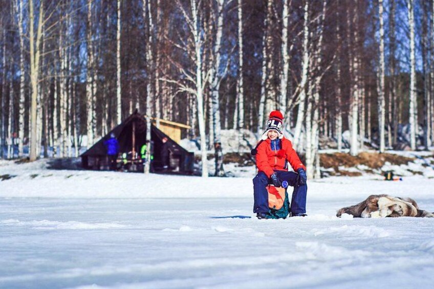 A person in a red jacket sitting on a sled in a snowy forest with a cabin in the background. 5