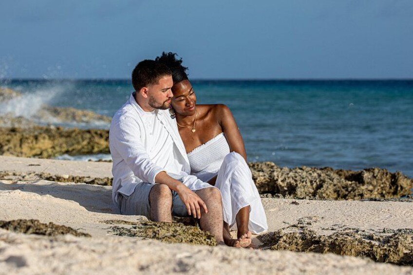 A couple sitting on a rocky beach with the ocean in the background. 2