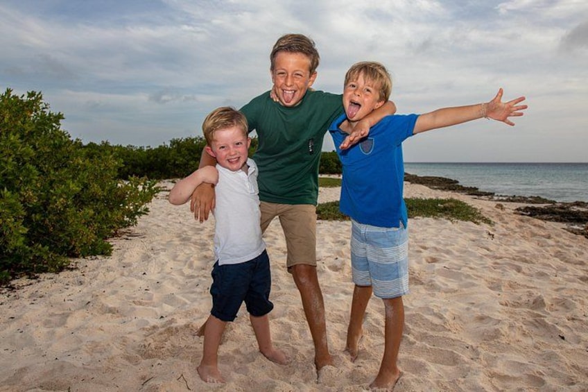 Three people on a sandy beach with vegetation and the ocean in the background. 3