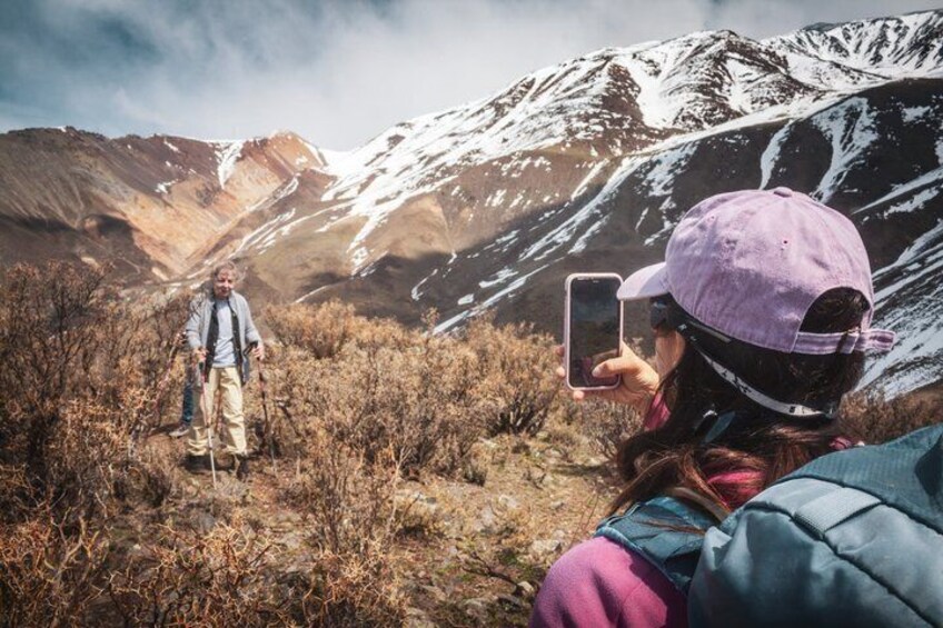 A person taking a photo of another person standing in a mountainous area with sparse vegetation. 5