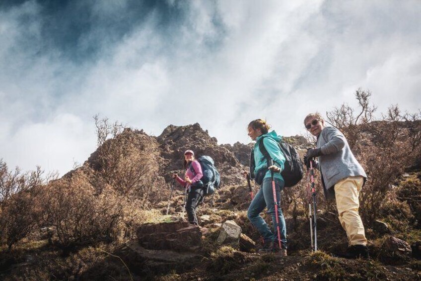 Hikers on a rocky mountain trail with sparse vegetation and a cloudy sky. 2