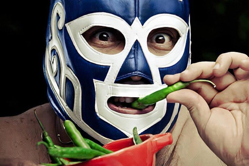 Una persona con una máscara azul y blanca, llevando un chile verde en la boca. 2