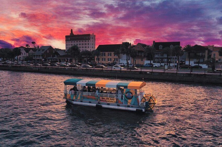 A riverboat with a blue and white canopy, a sign with contact information, and a sunset in the background. 2